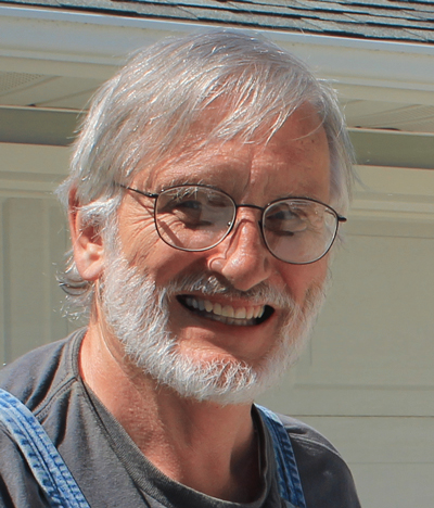 gray-bearded, smiling man wearing denim overalls